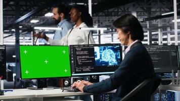 Data center technician managing AI systems using mockup PC. IT professional in tech startup office using artificial intelligence on green screen computer in server hub, camera A video
