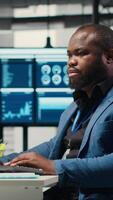vertikal afrikansk amerikan manlig analyserar finansiell data prognos på en dator, utvecklande innovativ företag lösningar för inriktning med företag mål. professionell miljö. kamera b. video