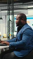 Vertical African american office worker leverages analytics and report writing for development and monthly performance results, resources and insights to ensure strategic goals achievement. Camera A. video