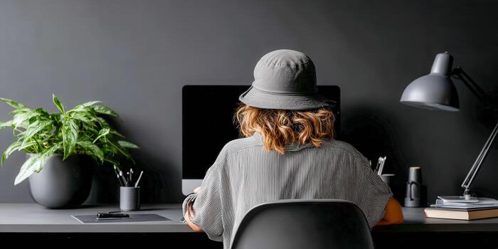 A woman wearing a hat sits at a desk with a computer photo