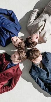Four men lie in a circle wearing suits in indoor studio photo