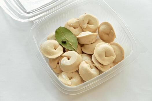 A close-up view of freshly prepared dumplings arranged neatly in a transparent container, showcasing their smooth texture and a hint of bay leaf for added flavor. photo