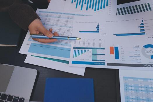 A person is using a pen to write on papers with graphs photo