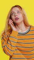 desinteresado rubia mujer teniendo irritado aburrido hablar en teléfono inteligente niña cansado soñoliento persona de libre dedicación hablando en móvil teléfono con amigo, haciendo en línea conversacion aislado en amarillo antecedentes video
