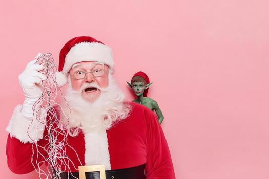 Santa Claus holding tangled string with surprised expression and elf behind on pink background photo