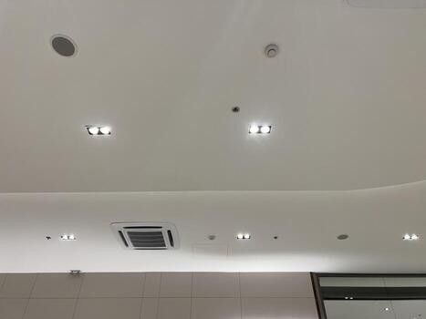Functional and modern white ceiling with recessed lighting, air conditioner, security camera, smoke detector, and speaker creating secure and comfortable atmosphere photo