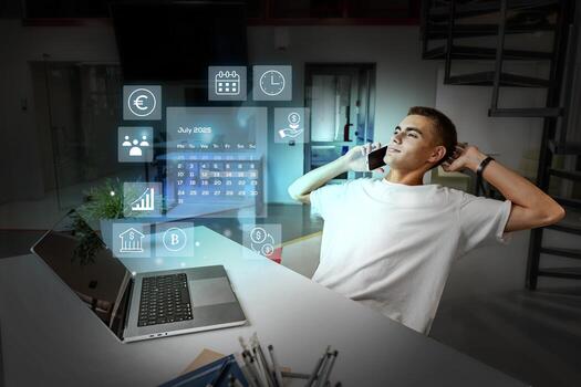 Young man engages in remote work while using a laptop and phone in a futuristic office setting during the evening hours photo