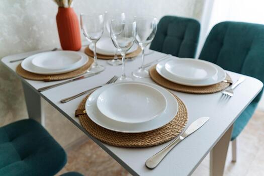 An incredibly elegant dining room table is meticulously and beautifully set with a stunning array of plates, fine glasses, and shiny silverware wonderfully artfully arranged on its surface photo