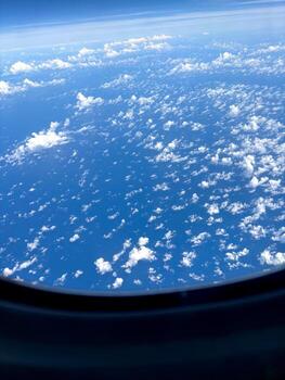 An aerial view captured from an airplane window. Puffy white clouds scatter across a deep blue sky, floating above the sea below. The image captures the nature of vast Pacific Ocean seen from above. photo