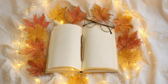 Cozy autumn flatlay with open notebook, pen, glasses, and fall leaves on soft fabric photo