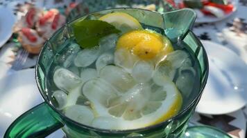 A refreshing pitcher of iced lemon water sits on a table, perfect for summer gatherings, picnics, and hydration includes sliced lemons and ice cubes video