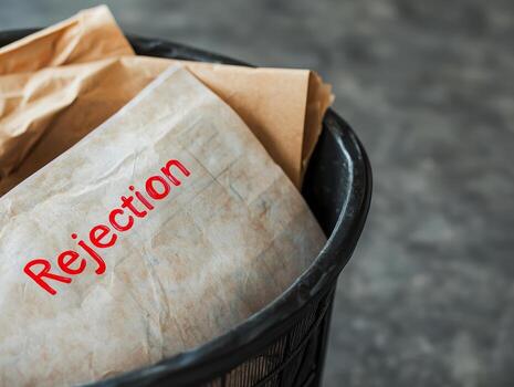 Rejection paper in trash bin with crumpled brown paper inside, symbolizing failure and discarded plans in blurred background photo