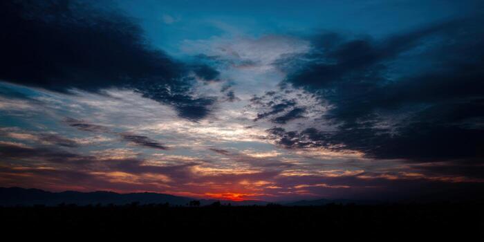 The setting sun casts a stunning glow over the mountains with vibrant clouds, creating a beautiful scene. photo