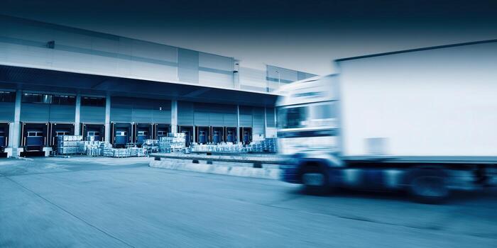 A fast-moving delivery truck passes a large warehouse loading dock, symbolizing efficient distribution. photo