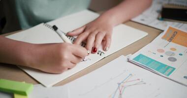 selectivo atención disparo, un mujer es tomando notas en un cuaderno mientras sentado a un escritorio lleno con negocio cartas y pegajoso notas video