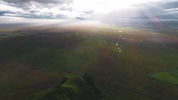 en lugn antenn se av grön fält och lindning strömmar i Island, med solljus strömning genom moln och gjutning dramatisk skuggor. video