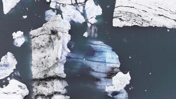 Aerial view of a glacial lagoon in Iceland with massive icebergs floating in deep blue water. The glides smoothly, showcasing intricate ice patterns. video