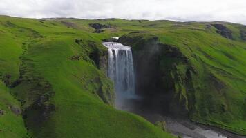 antenn se av skogafoss vattenfall i Island, cascading in i en dimmig slå samman. spår och vägar är synlig, med rullande kullar och avlägsen berg. video