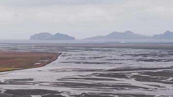 espansivo aereo Visualizza di intrecciato fiume modelli su un' piatto pianura con aspro montagne nel il distanza sotto un nuvoloso cielo nel Islanda. video