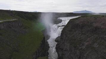 gullfoss cascata dentro Islândia fluxos sobre múltiplo camadas para dentro uma desfiladeiro, com névoa Aumentar e uma montanhoso pano de fundo debaixo uma nublado céu. video