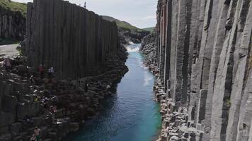 Studlagil Canyon in Iceland features towering basalt columns and a turquoise river. Water flows dynamically, cascading over a small waterfall. video