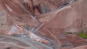 aéreo Visão do kerlingarfjoll e studlagil desfiladeiro - vibrante vermelho e laranja colinas, neve remendos, e vapor aberturas dentro Islândia. suave declives e córregos adicionar dinâmico elementos para a cena. video