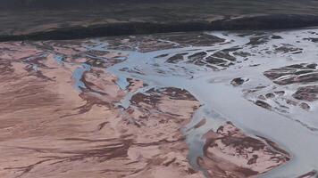 Aerial view of intertwining river channels flowing through a volcanic landscape in Iceland, with slow motion showcasing intricate patterns and terrain. video