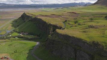 Aerial view of Seljalandsfoss waterfall in Iceland, with cascading water, lush green fields, a winding stream, and visitors on a walking path. video