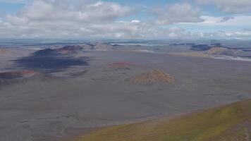 sotning antenn se av rödaktig vulkanisk kratrar på en karg enkel, omgiven förbi bergen under en delvis molnig himmel med rör på sig skuggor. video