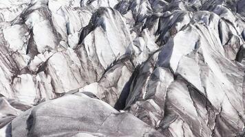 radicale aereo Visualizza di un' ghiacciaio nel Islanda, in mostra frastagliato ghiaccio formazioni, in profondità fessure, e ripido neve coperto montagne nel il sfondo. video