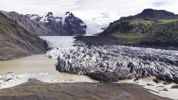 Aerial view of a glacier in Iceland with ice flow into a lagoon of icebergs, surrounded by cliffs and moss covered hills in a slow pan motion. video