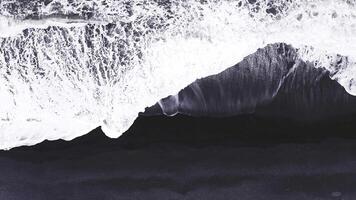 Aerial perspective of Iceland's black sand beach as waves crash onto the shore, highlighting the contrast between dark sand and white foam. video