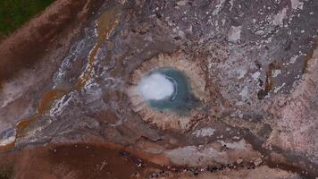 Aerial view of a steaming blue hot spring in Iceland, surrounded by mineral deposits and colorful runoff, with visitors adding scale to the scene. video
