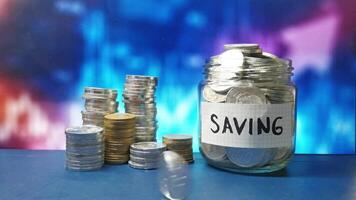 Coin rolling towards a pile of coins and jar full of coins with blurred background. This depicts the concept of saving and financial growth, symbolizing the accumulation of wealth. video