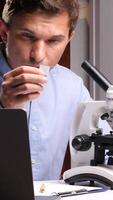 verticale scienziato analizzando campione diapositiva nel laboratorio con microscopio e il computer portatile video