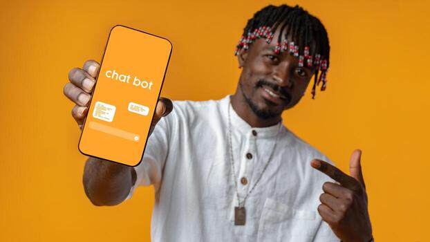 Man showcasing chatbot on smartphone against vibrant orange background while smiling and pointing photo
