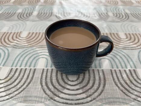 A closeup photo of navy blue coffee cup with brown speckles, resting on a modern tablecloth with a geometric Bauhaus-style pattern. The image combines minimalist design with retro-modern aesthetics.