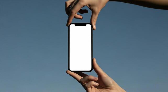 Two hands holding a modern smartphone with a blank white screen against a clear blue sky. photo