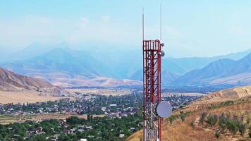 Drone footage showing a mountain village near with a telecom tower on a dry hill. The drone flying slowly down in front of the tower, creating a parallax effect with distant mountains in the background. video