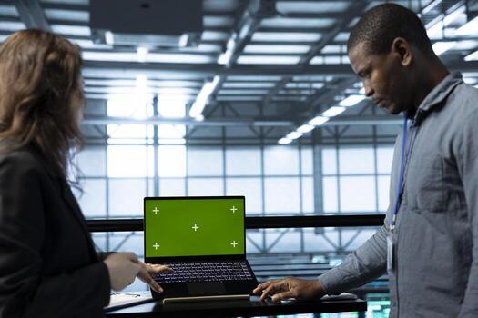 Admins using green screen laptop in data center, managing server virtualization. IT professionals using chroma key notebook in server room, sustaining long term infrastructure reliability photo