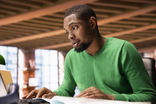 Man at home office desk crosschecking information between laptop screen and paper files, seeing inaccuracies. Remote worker confused by missing data in documents, comparing with notebook display photo