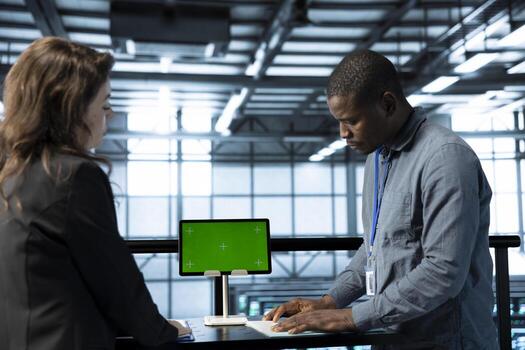 System administrators in data center using isolated screen mockup tablet to verify settings. African american man and colleague using green screen chroma key device used by workers in server farm photo
