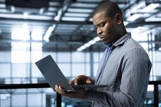 Technician in data center with laptop integrating AI driven automation tools, running predictive maintenance routines, analyzing operational metrics, ensuring continuous uptime, managing data flows photo