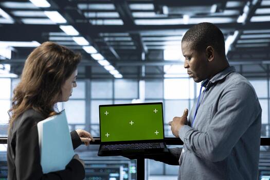 Team of engineers in data center using green screen laptop to do network virtualization. Coworkers in server farm using chroma key notebook, updating storage arrays, verifying settings photo