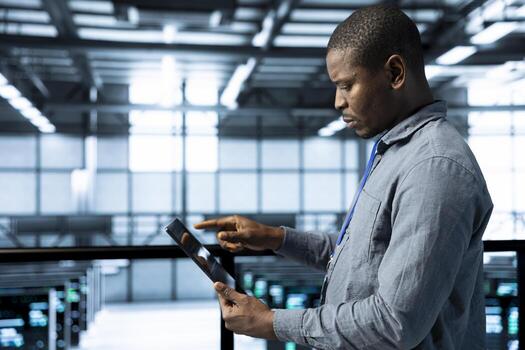 Admin in data center using tablet to deploy new server architectures, configuring network virtualization. Man in server room updating storage arrays, verifying settings to maintain stable performance photo