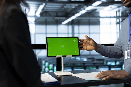 Admins in data center use mockup tablet, inspecting server rackmounts, updating network topologies, close up shot. IT specialists talking, using chroma key device, ensuring stable operations photo