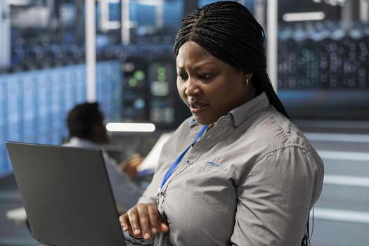 System administrator in server room using laptop to implement and manage data backup solutions. Data center IT expert identifying and resolving technical errors, ensuring efficient recovery photo