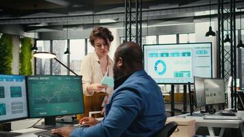 Workplace support employee moves a delivery cart stacked with folders and contracts, helping african american administrator bringing stack of archived documents for accounting tasks. Camera B. video