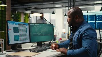 Black employee building new development strategy with notes, analyzing data and solutions to forecast project outcomes. Male professional working on briefing reports in the office. Camera A. video