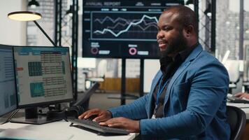 svart anställd använder sig av data och teknologi för företag förvaltning, granskning påstående grafer på övervaka till skapa rapporter och förbättra effektivitet, mål prestation. syn. kamera b. video